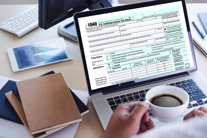 Martinson & Carter, CPAs, PA | close-up of a laptop monitor with 1040 tax information with a hand holding a cup off coffee over the keyboard with folders and books on a desk